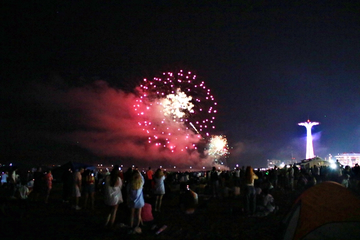 Independence Day fireworks with observers and the Parachute Jump to the right in the distance.